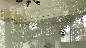 Une chambre à coucher avec un lit, un lustre, un climatiseur fixé au mur et une fenêtre donnant sur des arbres.