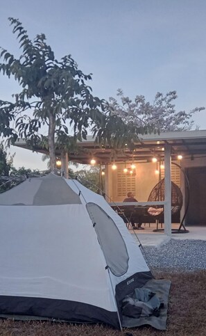 Une tente installée à l’extérieur, avec une table et des chaises placées sous une zone abritée, le tout illuminé par des guirlandes lumineuses.