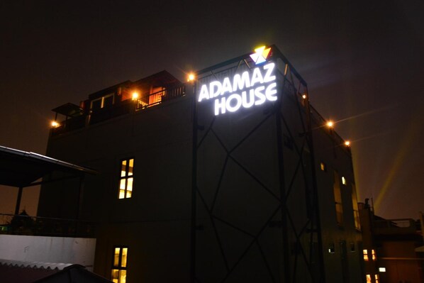 A building with a prominent sign reading "ADAMAZ HOUSE" at night.