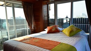 A hotel room with a large bed, a balcony with a view, and a wooden interior. - Adamaz House (Bangkok)