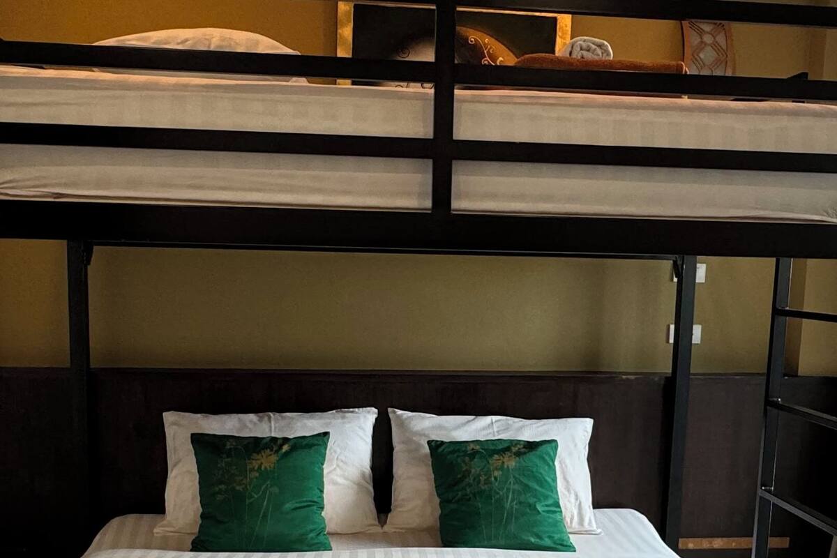 A bunk bed with a lower bed and a higher bunk. The lower bed has a green blanket and two pillows.