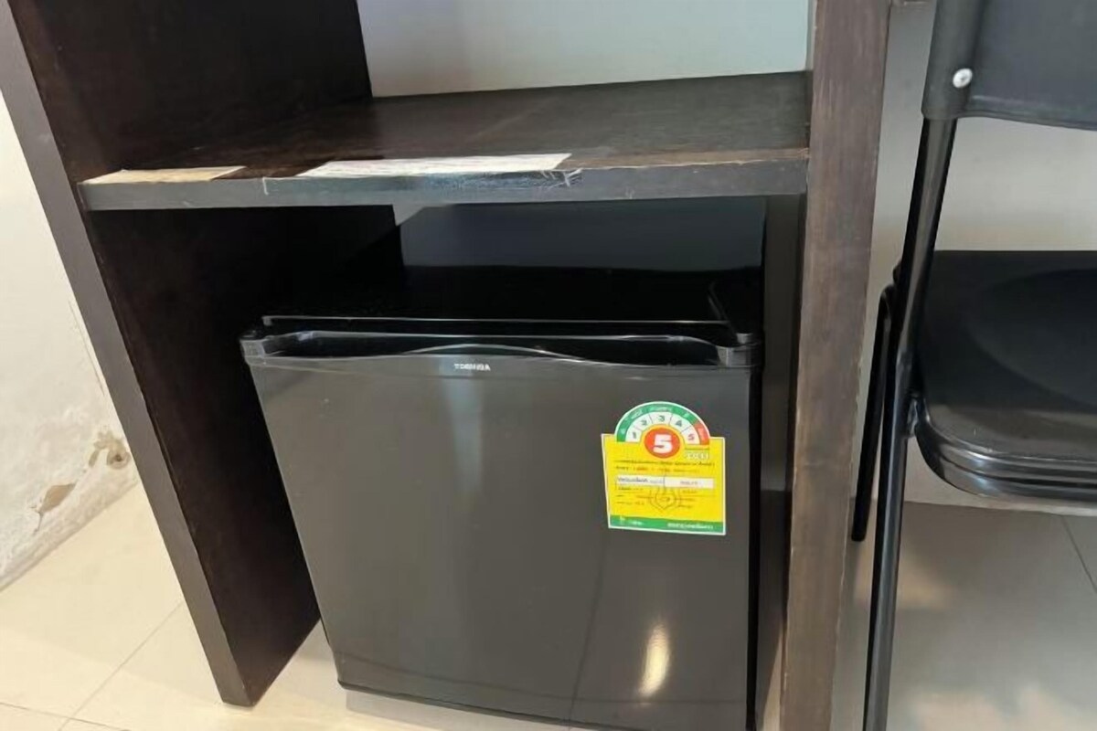 A compact refrigerator with a sticker indicating a 5-star rating, placed under a wooden shelf in a room with tiled flooring.
