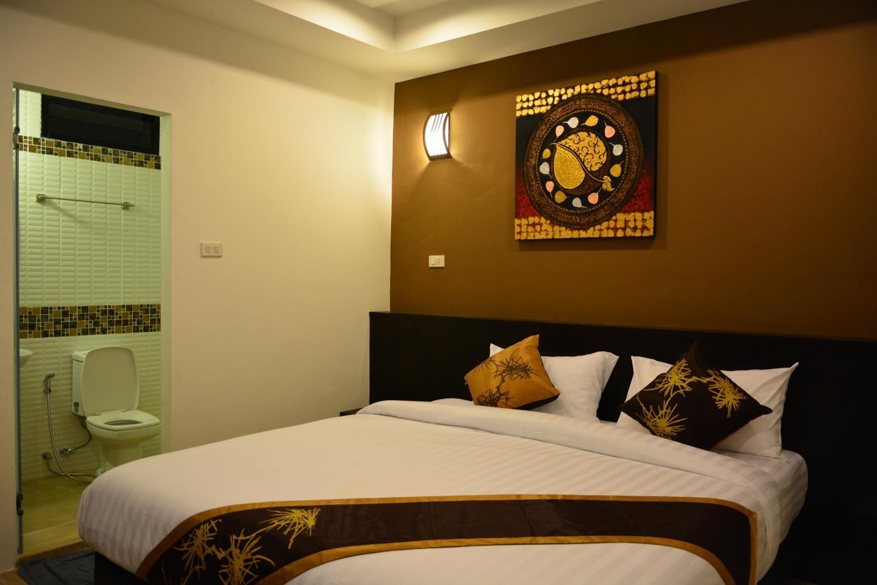 Una habitación de hotel con una cama, una obra de arte colgada en la pared y un baño visible a través de una puerta abierta.
