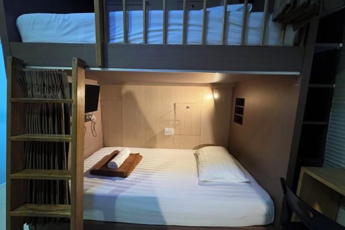 A bunk bed room with a wooden ladder, a bedside table with a book, and a small shelf.