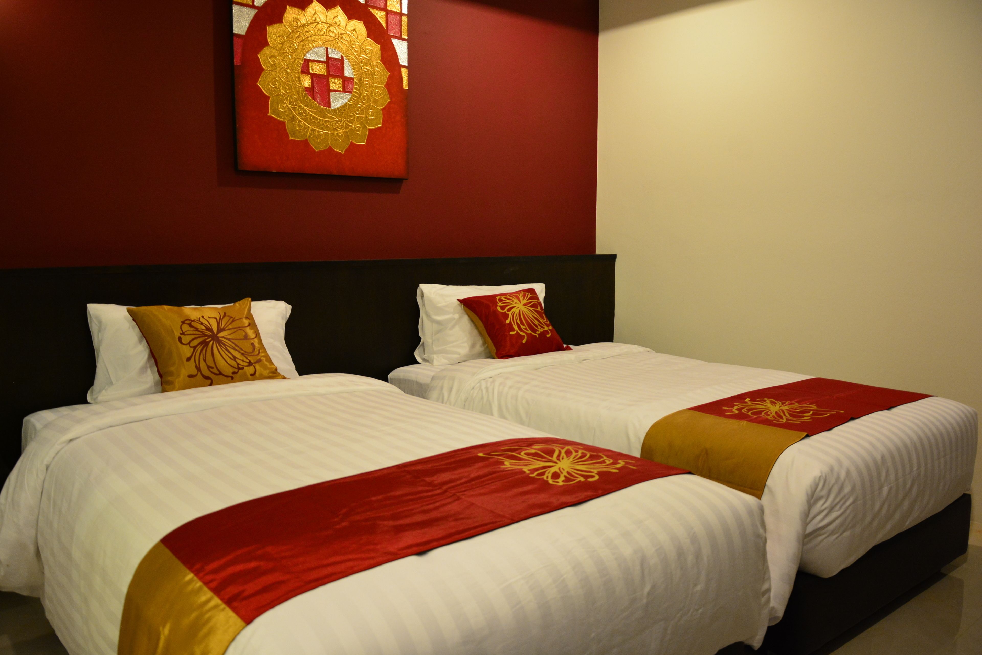 A hotel room with two beds, each with white bedding and red and gold accents.