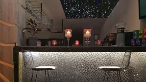 Uma área de bar com dois bancos, parede de azulejos em mosaico e teto com luzes que lembram estrelas.