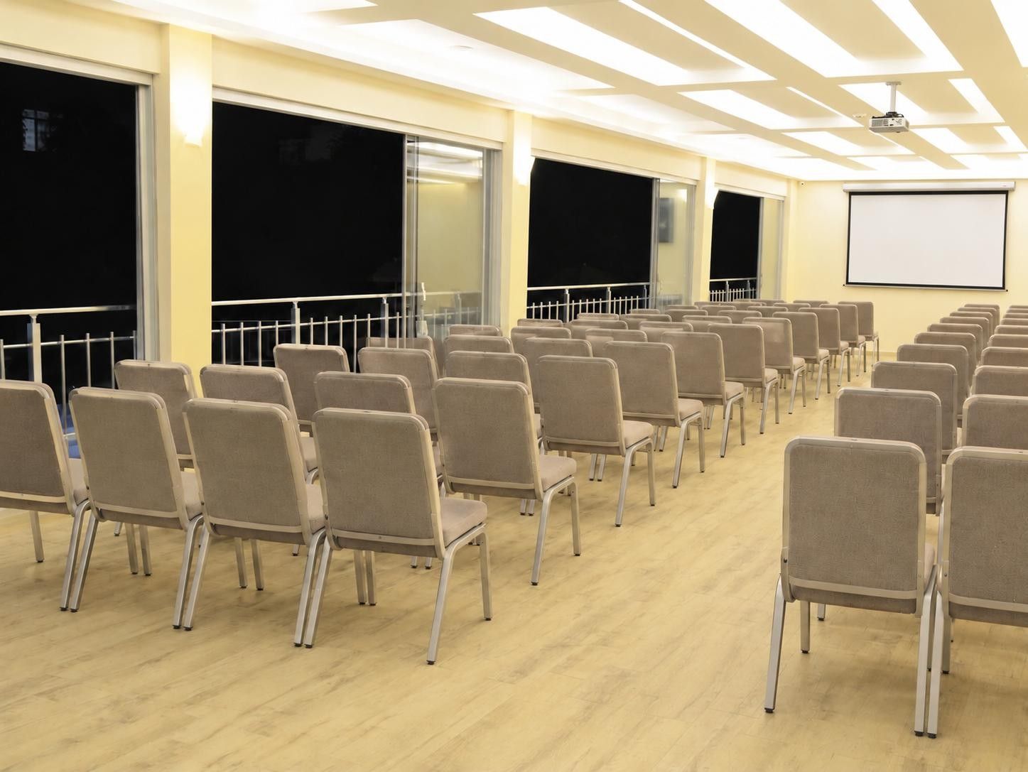A conference room with rows of chairs, large windows, and a projection screen.