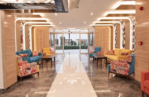 A lobby with a central glass partition, seating areas with patterned cushions, and a polished marble floor. - Ozgur Bey Spa Hotel (Alanya)