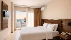 Quarto de hotel com uma cama, uma mesa de cabeceira com telefone e controle remoto, uma TV na parede e vista para o mar através de uma grande janela.
