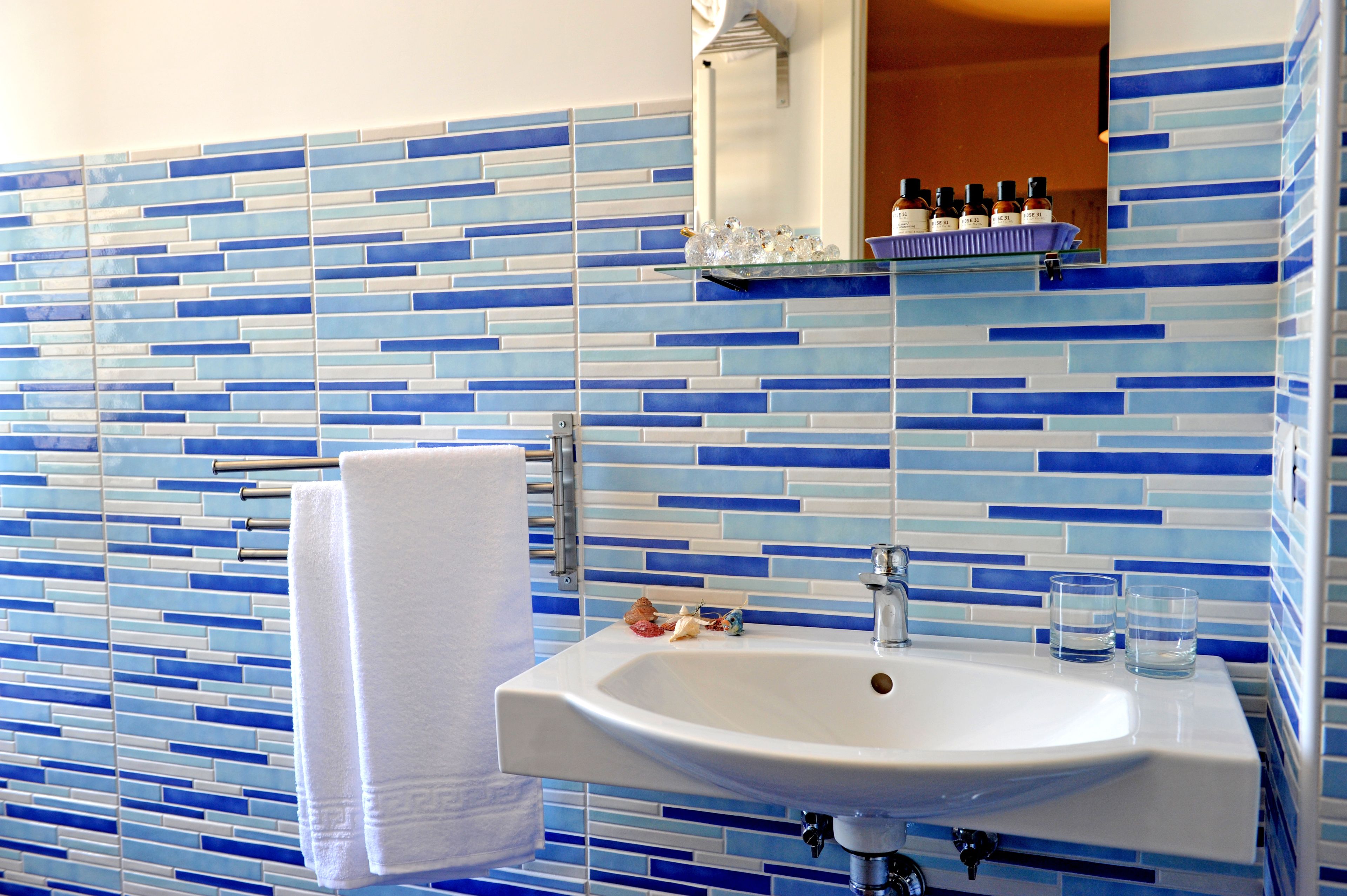 Um banheiro com mosaico azul e branco na parede acima da pia, uma pia branca, um porta-toalhas e um espelho sobre a pia.