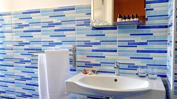 Um banheiro com mosaico azul e branco na parede acima da pia, uma pia branca, um porta-toalhas e um espelho sobre a pia.