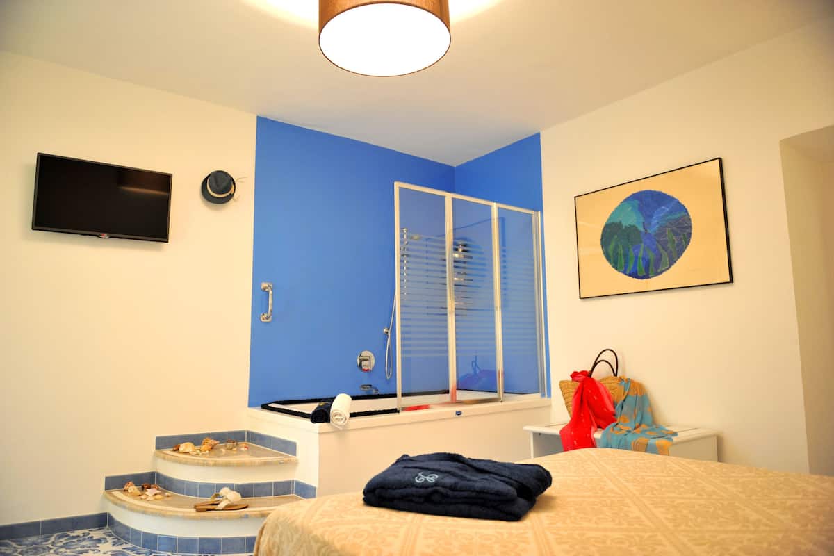 A hotel room with a blue accent wall, a bathtub, a flat-screen TV, and a framed artwork.