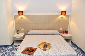 Ein ordentlich eingerichtetes Schlafzimmer mit einem gemusterten Bettbezug, zwei Nachttischen mit Lampen und einer dekorativen Vase auf einem Tisch.