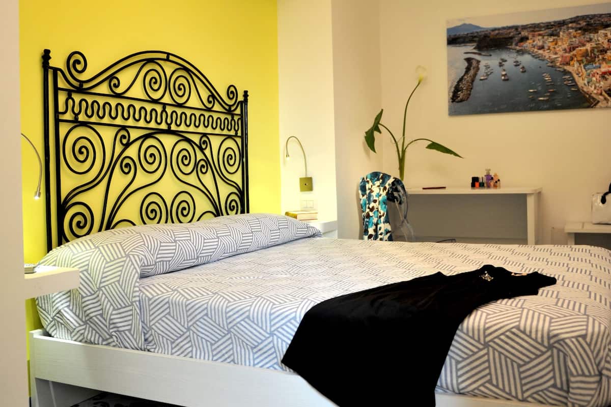 A bedroom with a bed, a nightstand, a vase with flowers, and a painting on the wall.