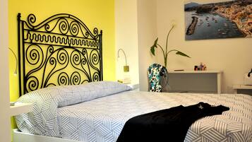 Um quarto com uma cama, uma mesa de cabeceira, um vaso com flores e um quadro na parede.