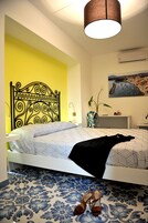 Um quarto com uma cama, uma mesa de cabeceira, um vaso com flores e um quadro na parede.