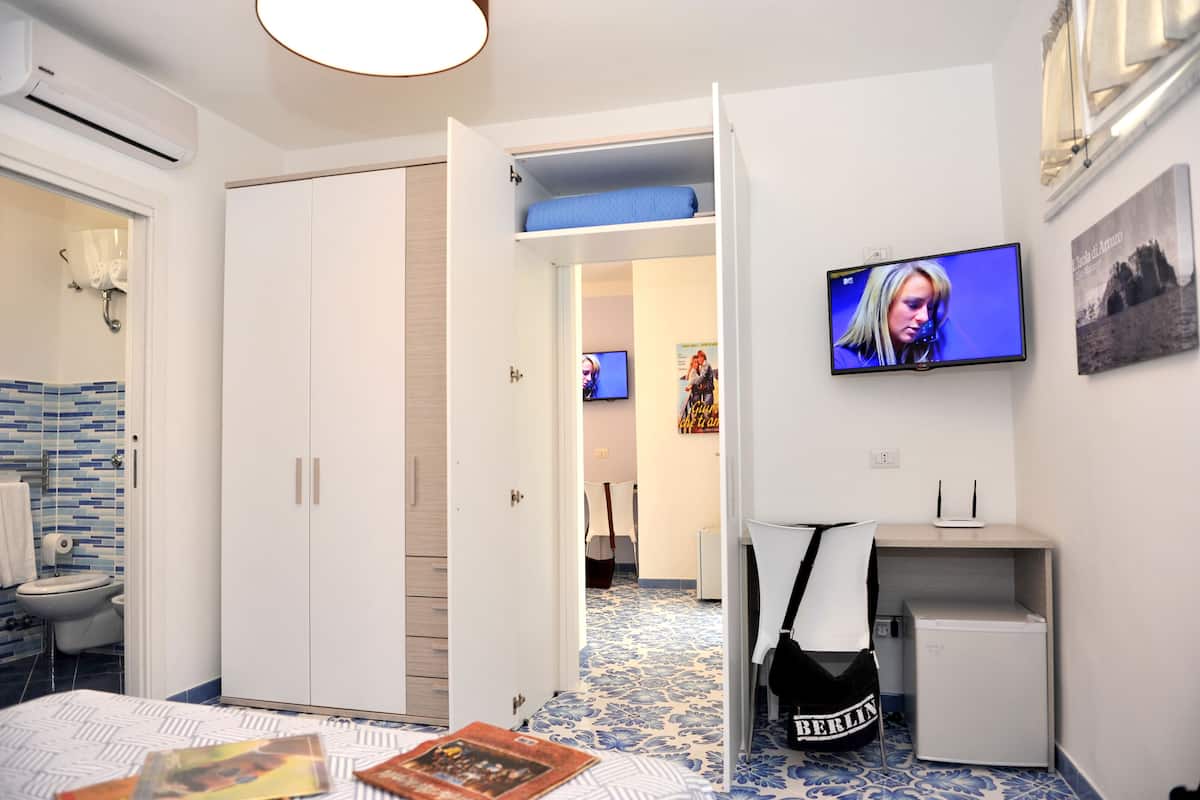 A hotel room with a bed, a TV, a desk with a computer, and a wardrobe.