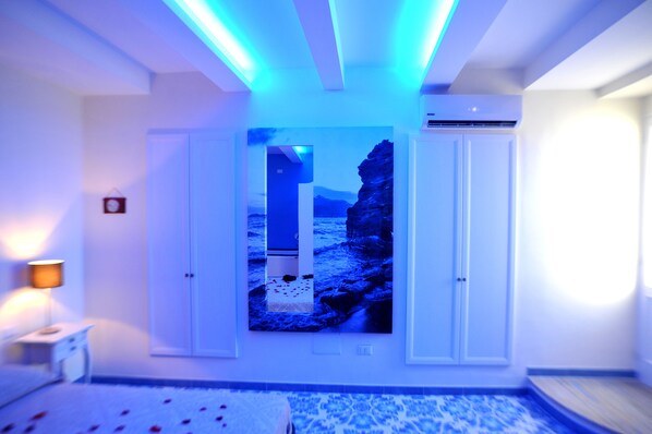 A room with a bed, a nightstand, a wall-mounted air conditioner, and a framed picture of a rocky landscape.