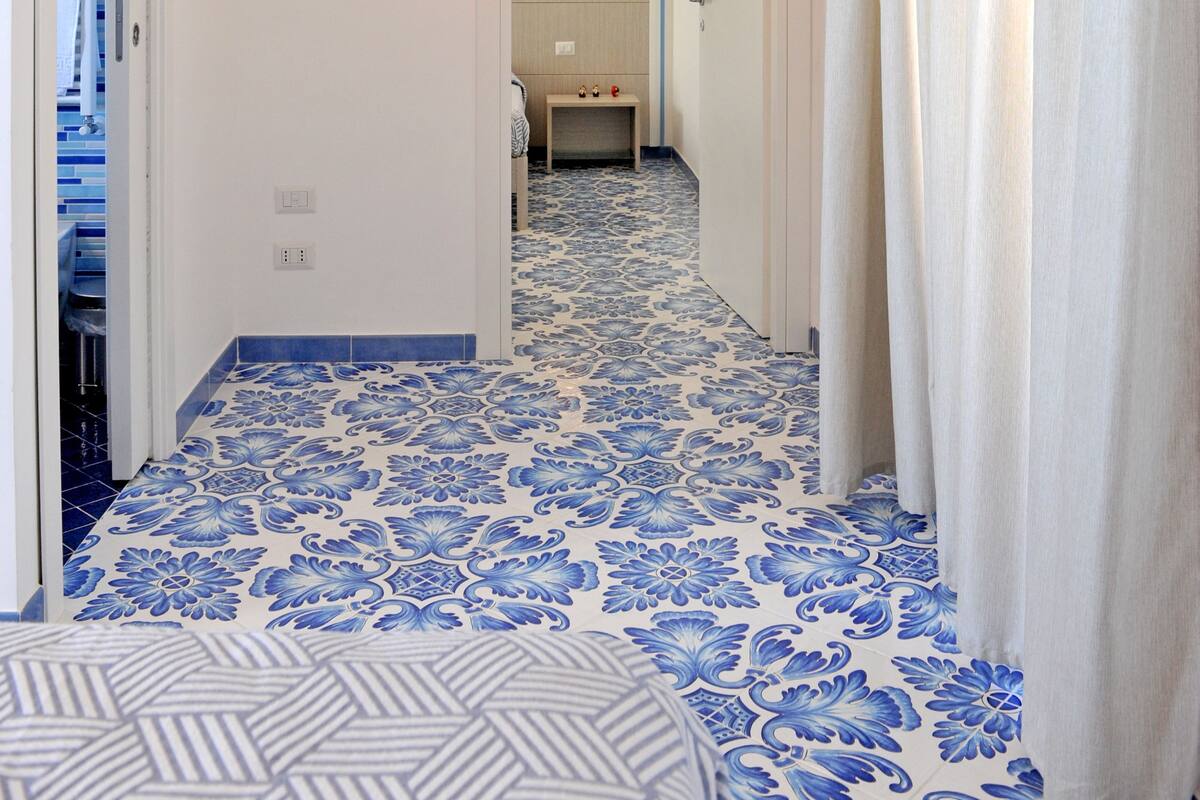 A hallway with patterned blue and white tiles, a ceiling light, a door leading to a bathroom, and a curtain on the right.