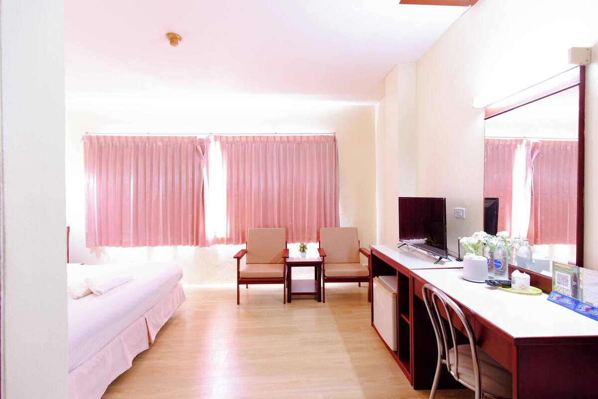 A hotel room with a bed, a desk, a chair, a TV, and a window with curtains.
