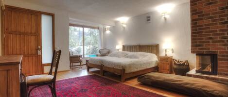 Una camera da letto con un letto, una sedia di legno, un tappeto rosso con motivi, un caminetto e vista sull'esterno.