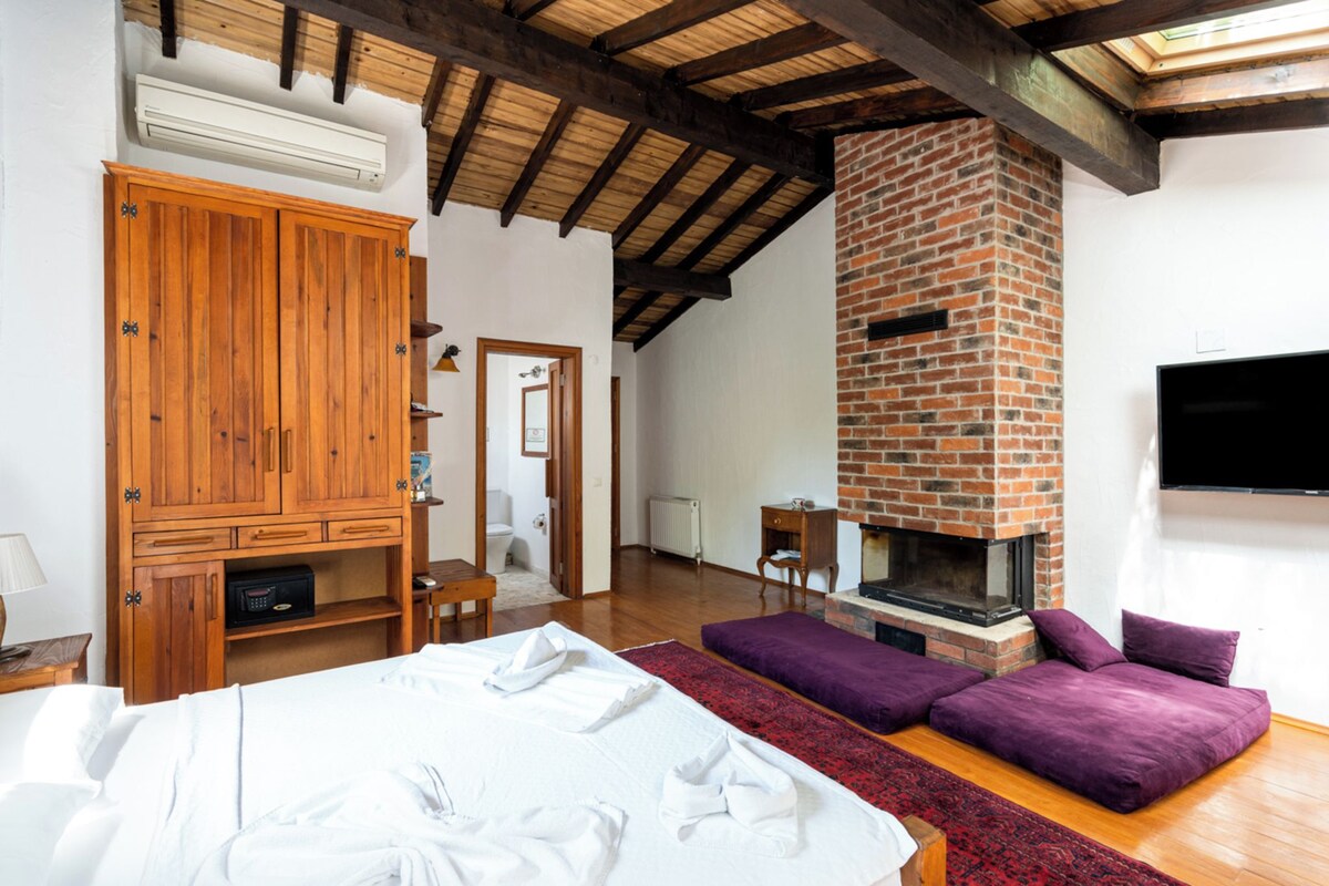 A room with a bed, a wooden wardrobe, a brick fireplace, and a television mounted on the wall.