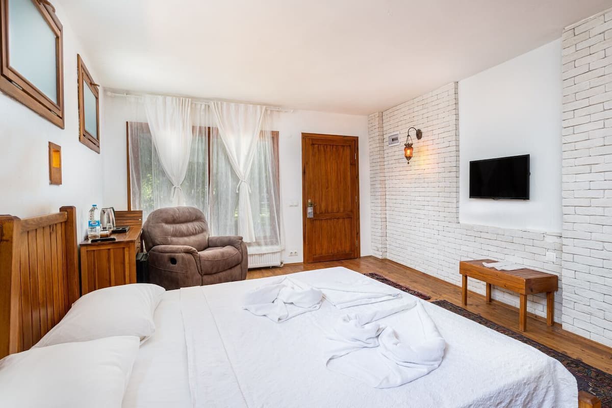 A hotel room with a bed, a chair, a television, and a brick wall.