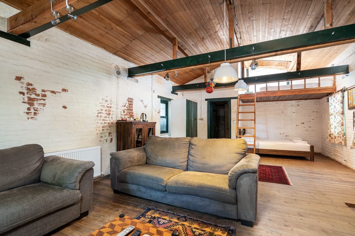 A rustic interior with exposed brick walls, wooden beams, a loft bed, and a sofa.