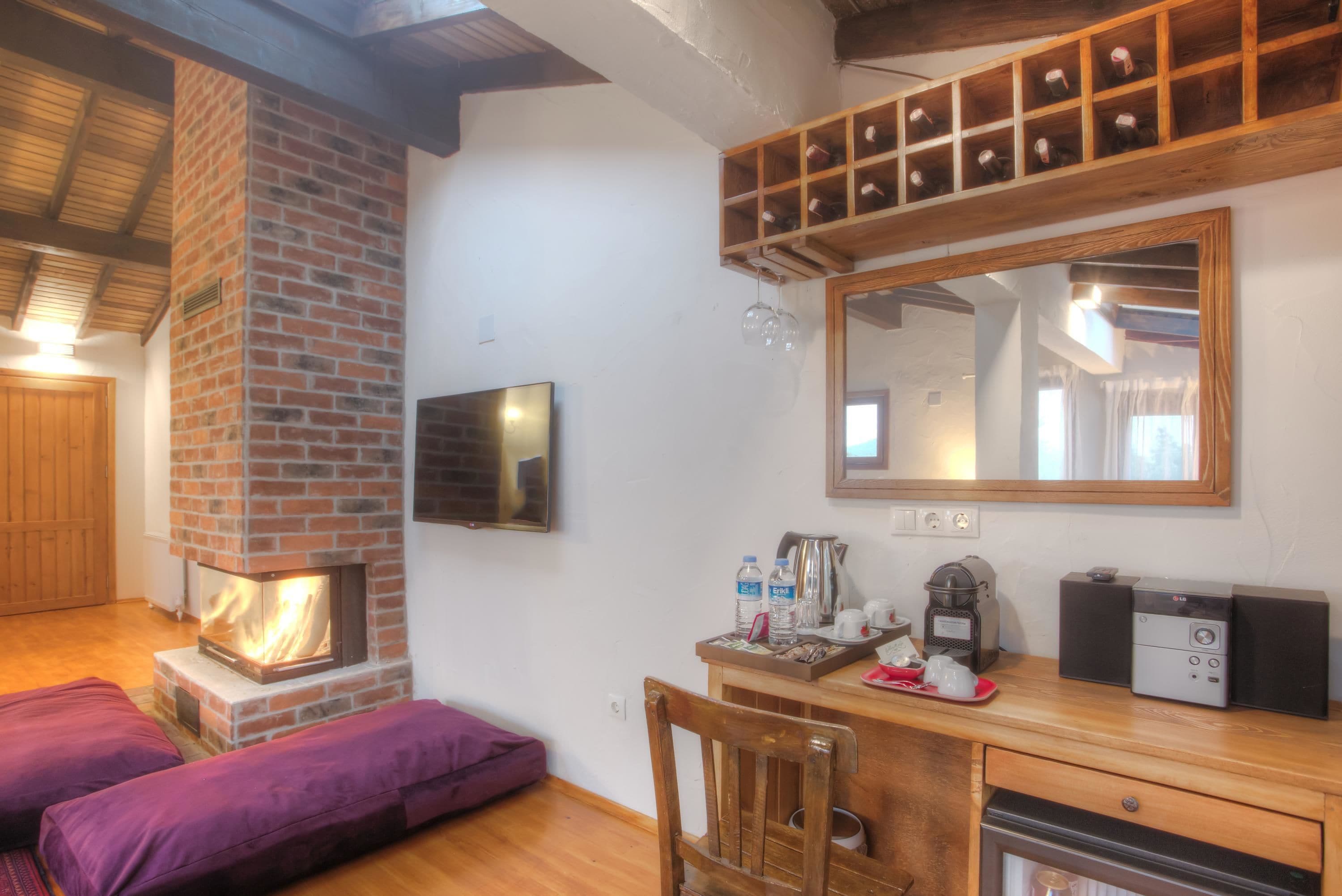 A cozy room with a brick fireplace, wooden furniture, a mirror, and a shelf with bottles.