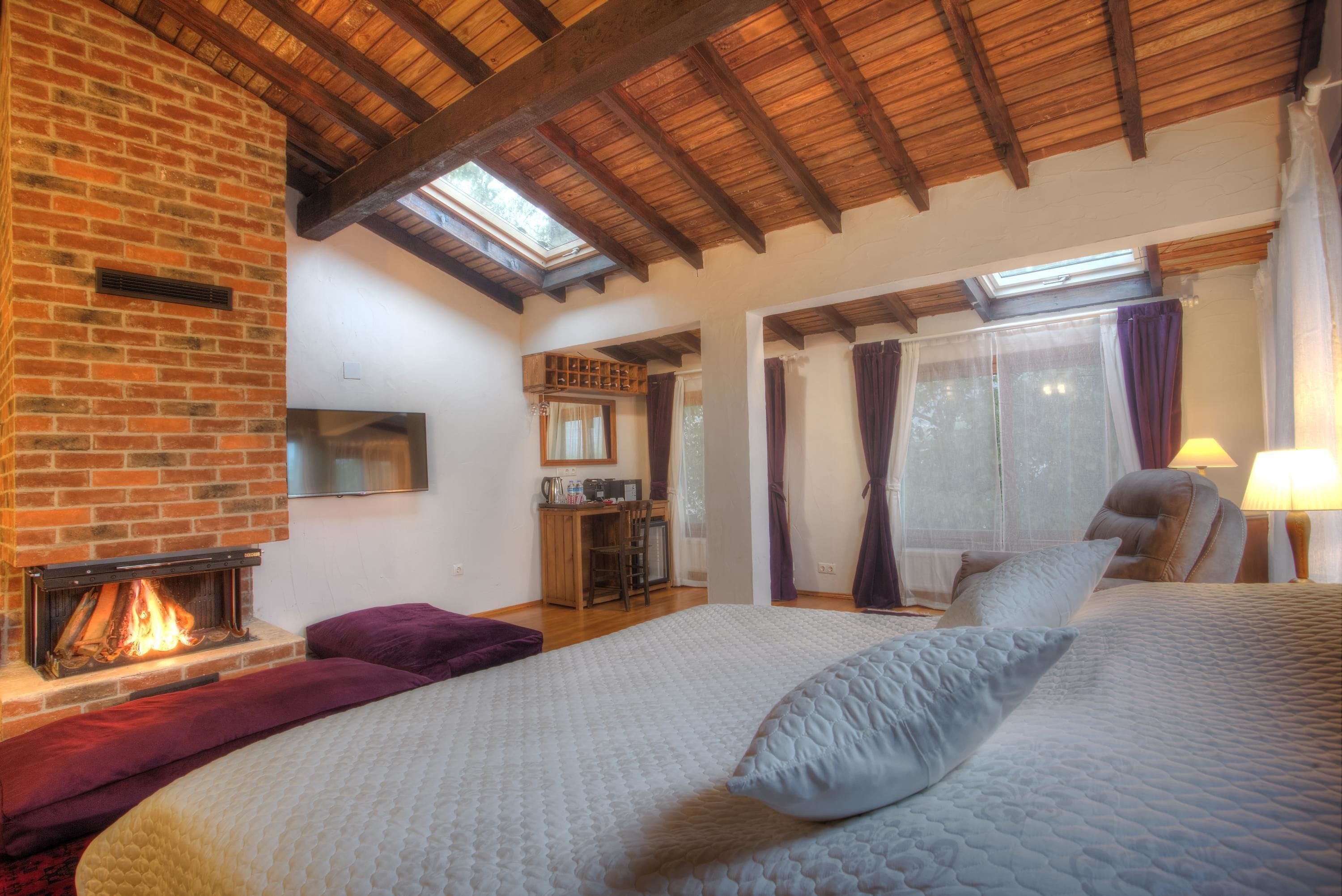 A bedroom with a fireplace, a bed with pillows, a desk, and a chair.