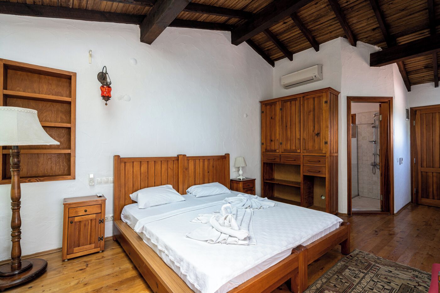 A bedroom with a wooden bed, a nightstand, a wardrobe, and a shower area.