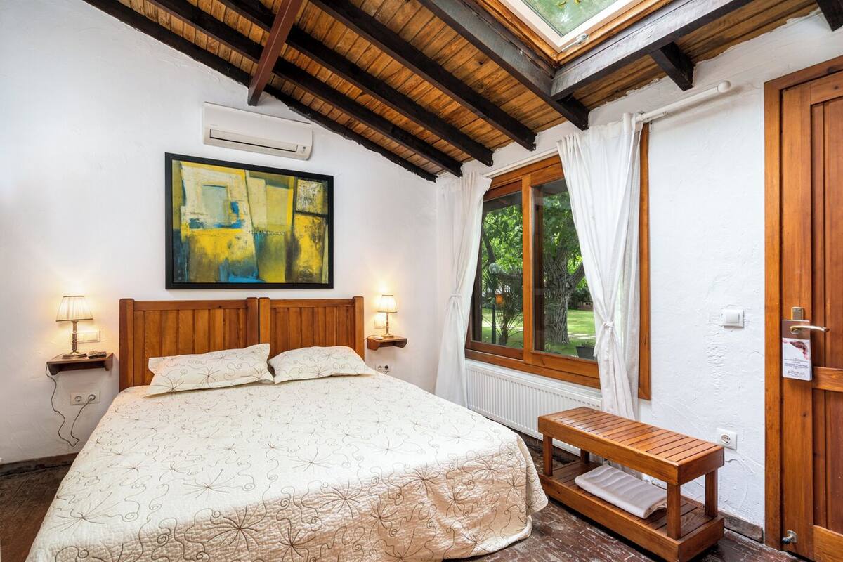 A bedroom with a wooden bed, a bedside table, a window with curtains, and a skylight.