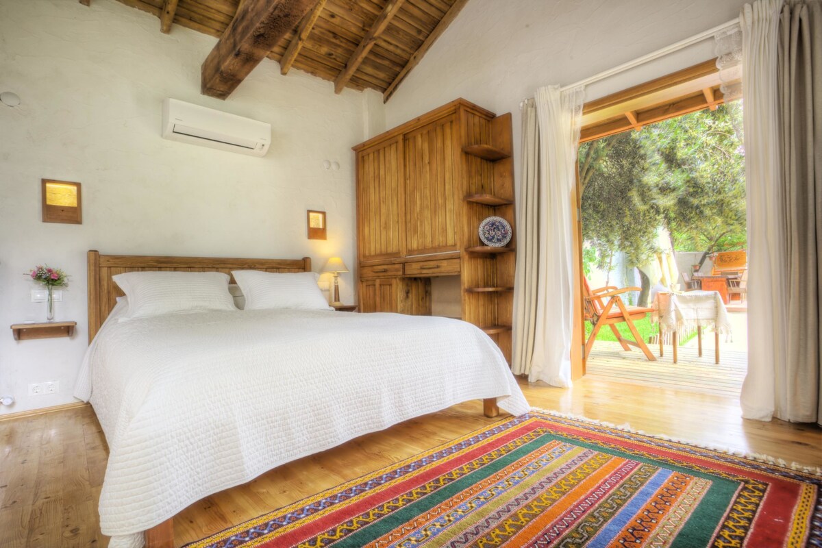 A bedroom with a wooden bed, a colorful rug, a wooden wardrobe, and a view of the outdoors.