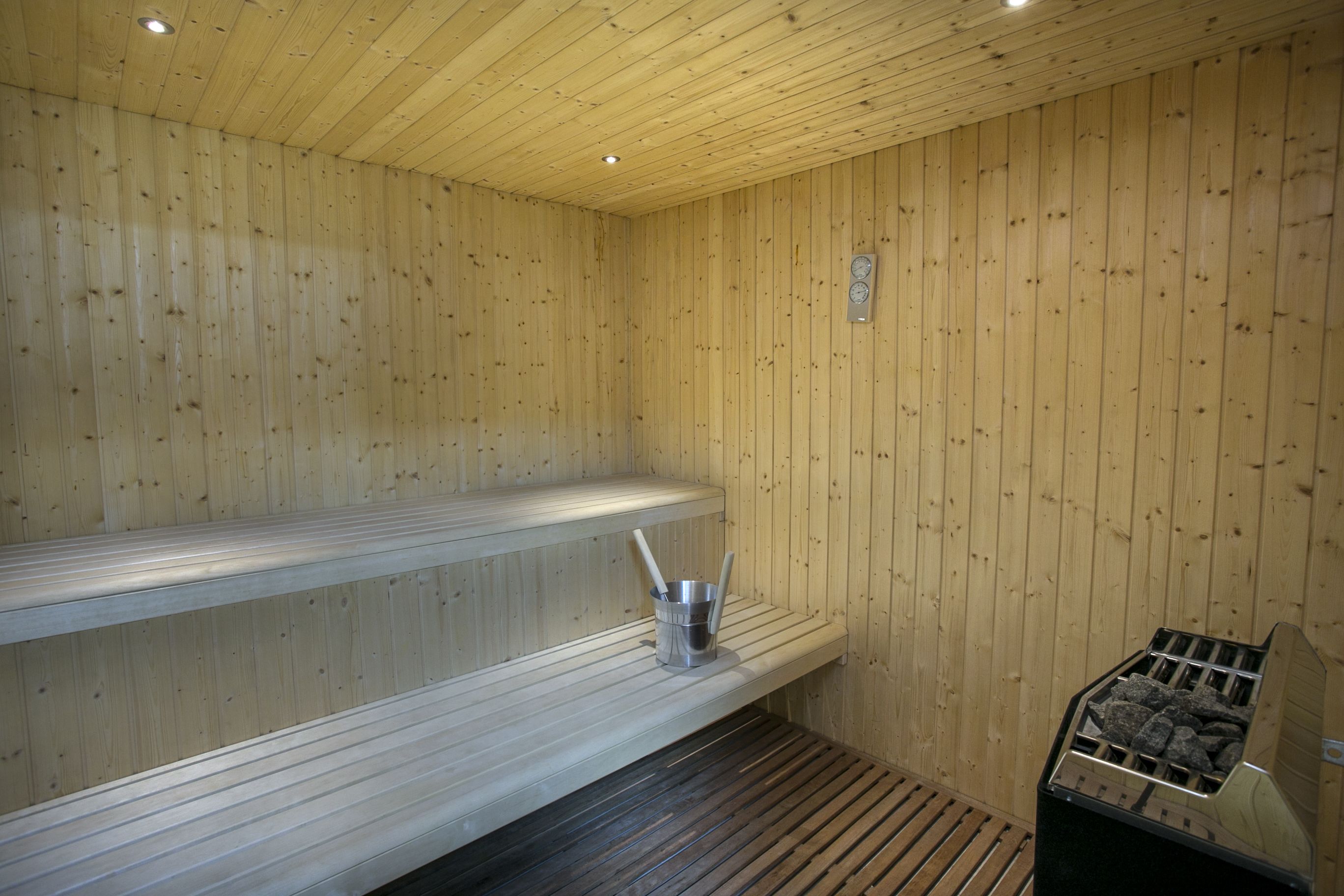 A sauna with wooden walls and benches, a metal bucket, and a sauna heater.