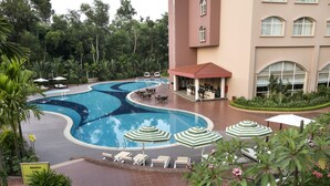 A swimming pool with lounge chairs and umbrellas, surrounded by greenery and a building with a red roof. - Grand Sultan Tea Resort & Golf (Kamalganj)