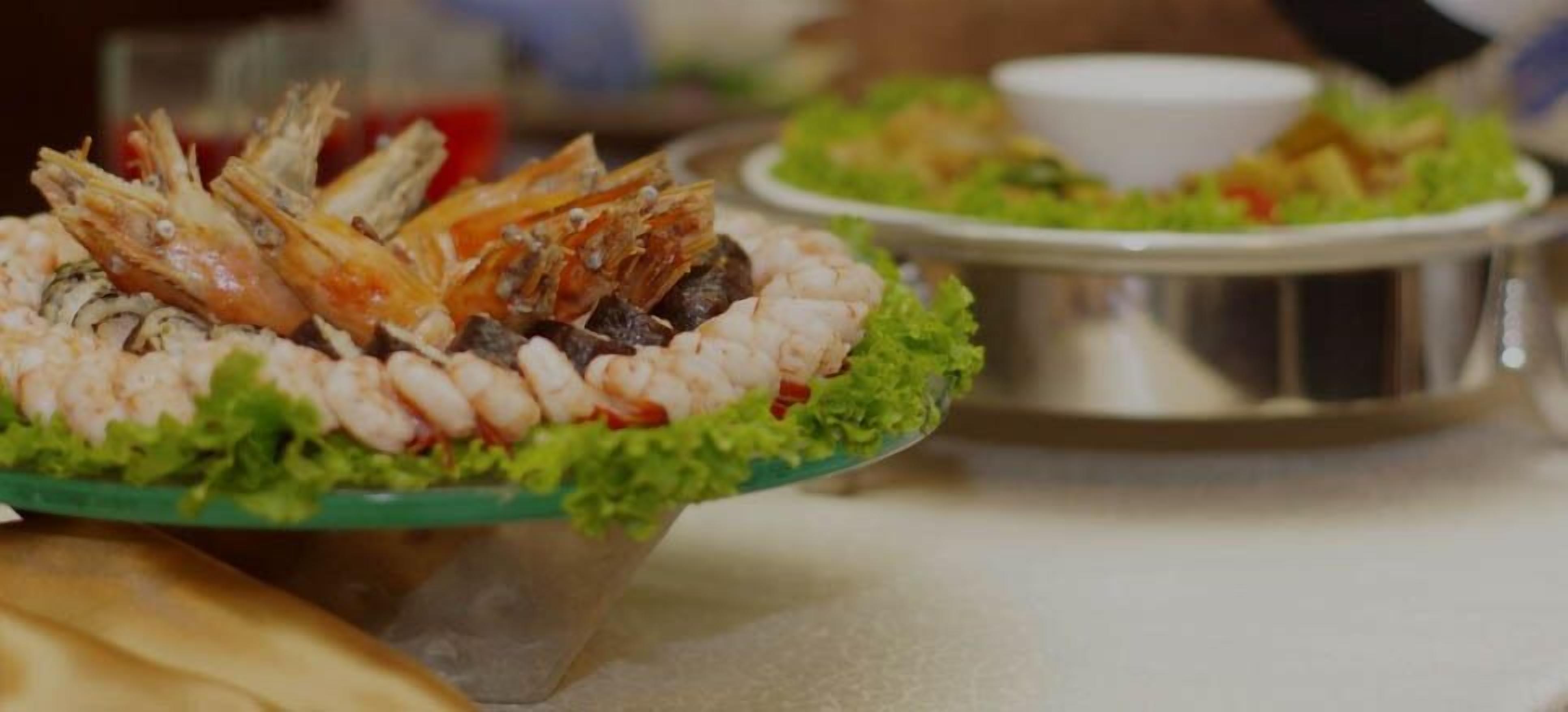 A seafood platter with shrimp and fish on a bed of lettuce, accompanied by a small bowl of sauce.