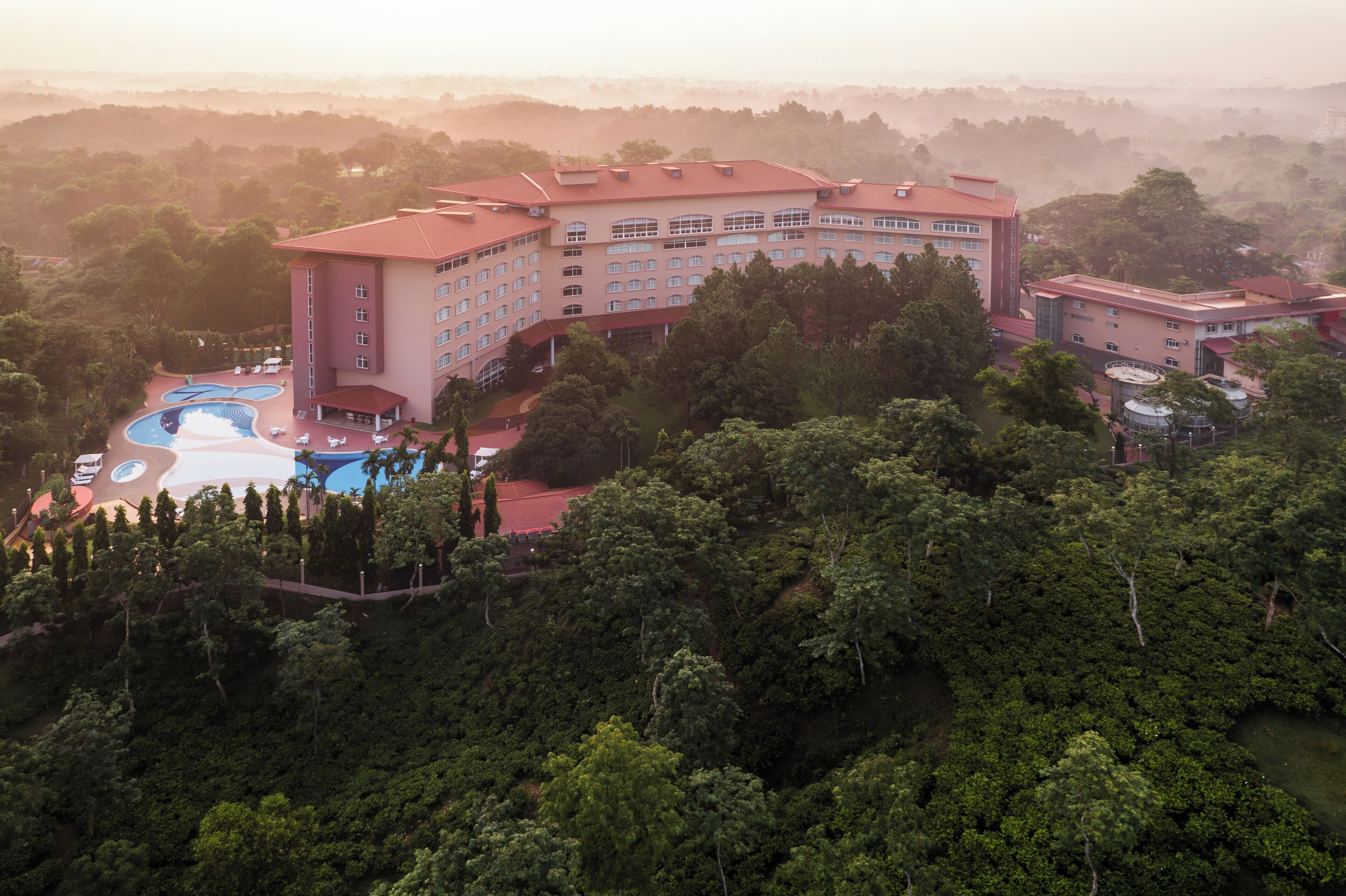 A large hotel with multiple buildings, a swimming pool, and lush surrounding greenery.