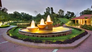 A circular water feature with multiple fountains, surrounded by a landscaped garden with a paved walkway. - Grand Sultan Tea Resort & Golf (Kamalganj)