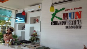 Mostrador de recepción en el Khuan Chaueng Resort con un televisor, aire acondicionado y una estatua decorativa.