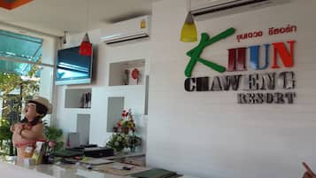 Mostrador de recepción en el Khuan Chaueng Resort con un televisor, aire acondicionado y una estatua decorativa.