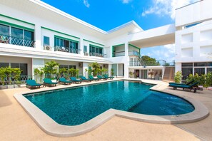 A swimming pool with lounge chairs, a white building with balconies, and a clear blue sky. - Khun Chaweng Resort (Koh Samui)