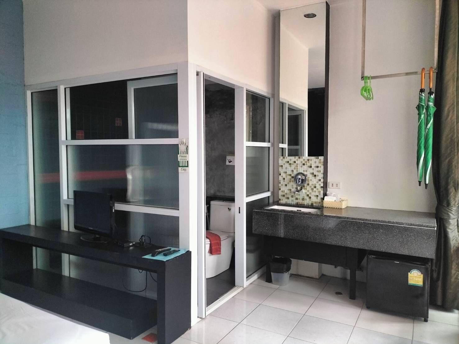 A modern bathroom with a black countertop, a mirror, and a green umbrella hanging on the wall.