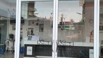 Zona de recepción con puertas de cristal, un letrero de bienvenida y piso de baldosas.