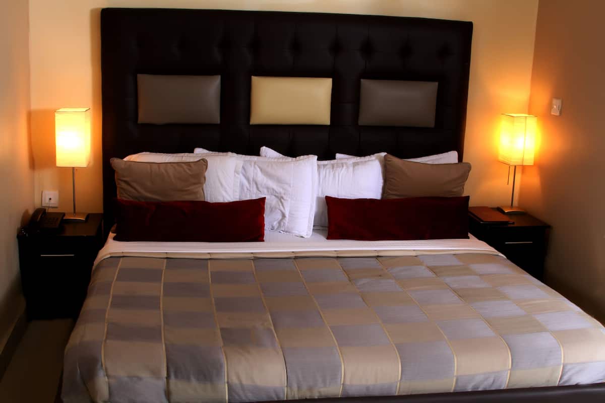 Una cama bien hecha con una colcha a cuadros, dos lámparas de noche y un cabecero oscuro.