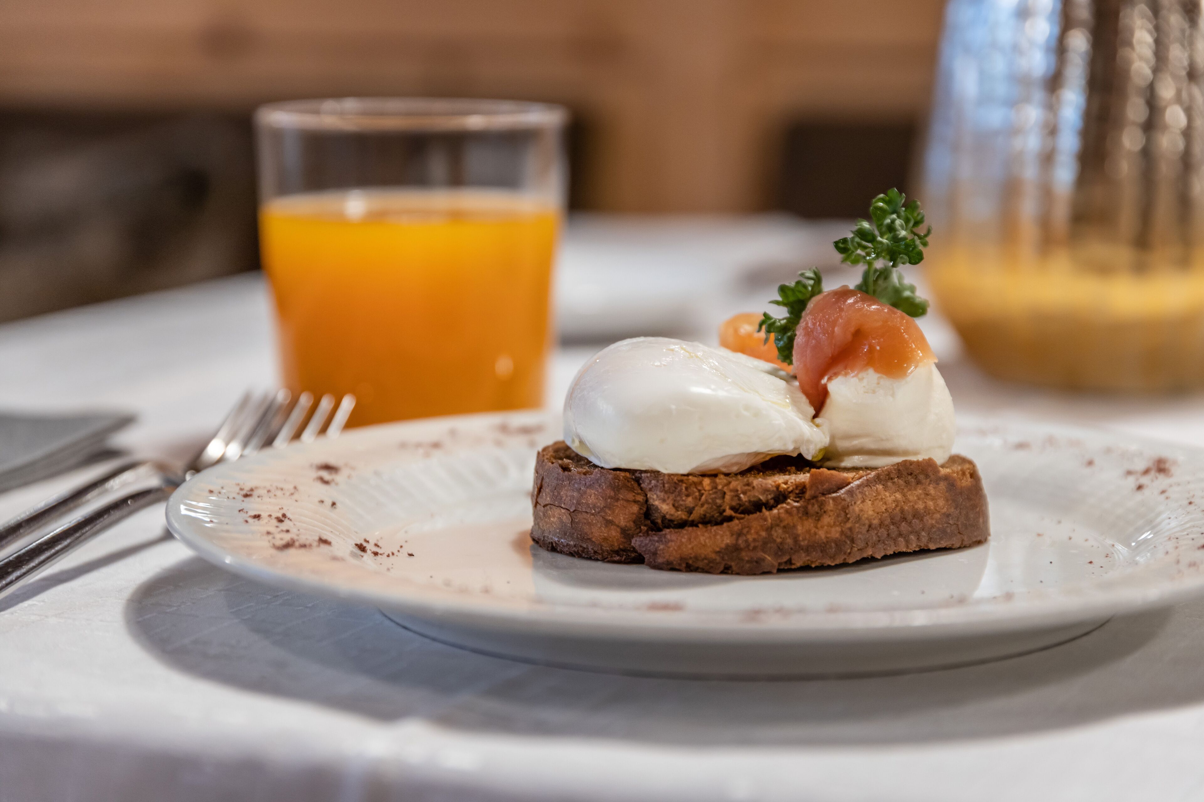 Een ontbijt bord met een gepocheerde eitje, gerookte zalm en garnering, vergezeld van een glas sinaasappelsap.