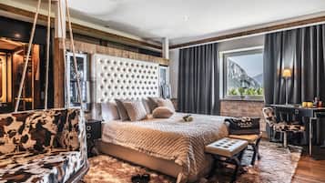 A modern bedroom with a large bed, a sofa, a desk, and a view of mountains.