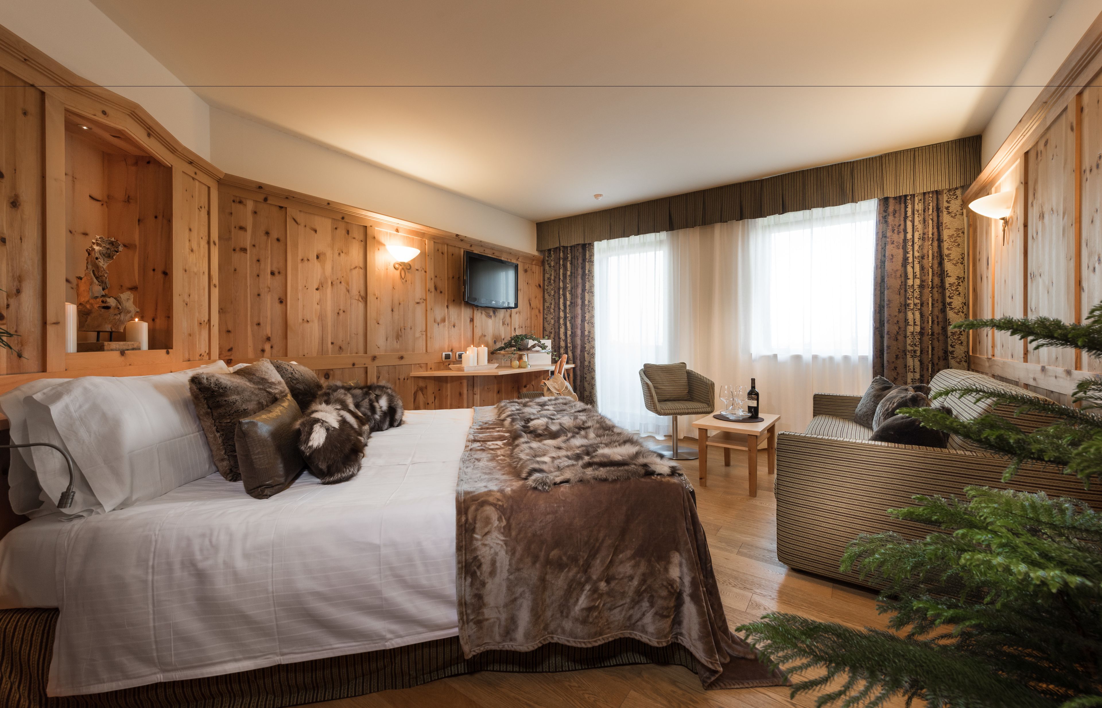 Una camera accogliente con un letto grande, un divano, un tavolino e un televisore fissato alla parete in legno.