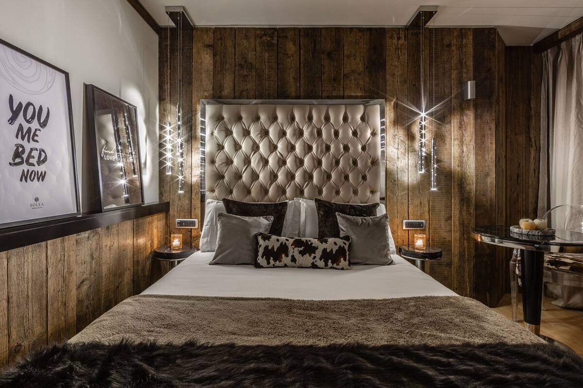 Een moderne slaapkamer met een gestoffeerd hoofdeinde, een zacht tapijt en een nachtkastje met een kaars.