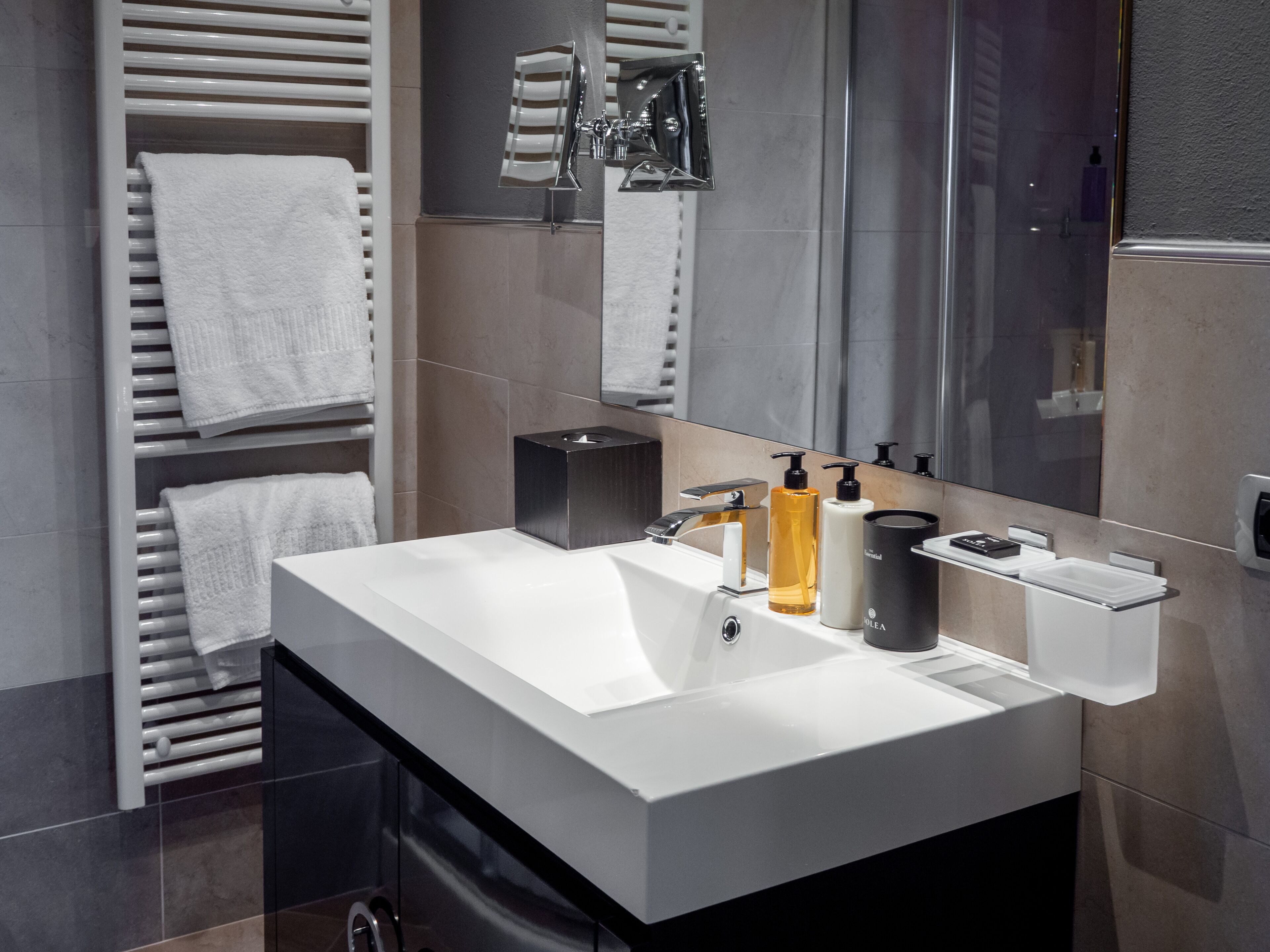 A modern bathroom with a large mirror, white sink, and towel racks.