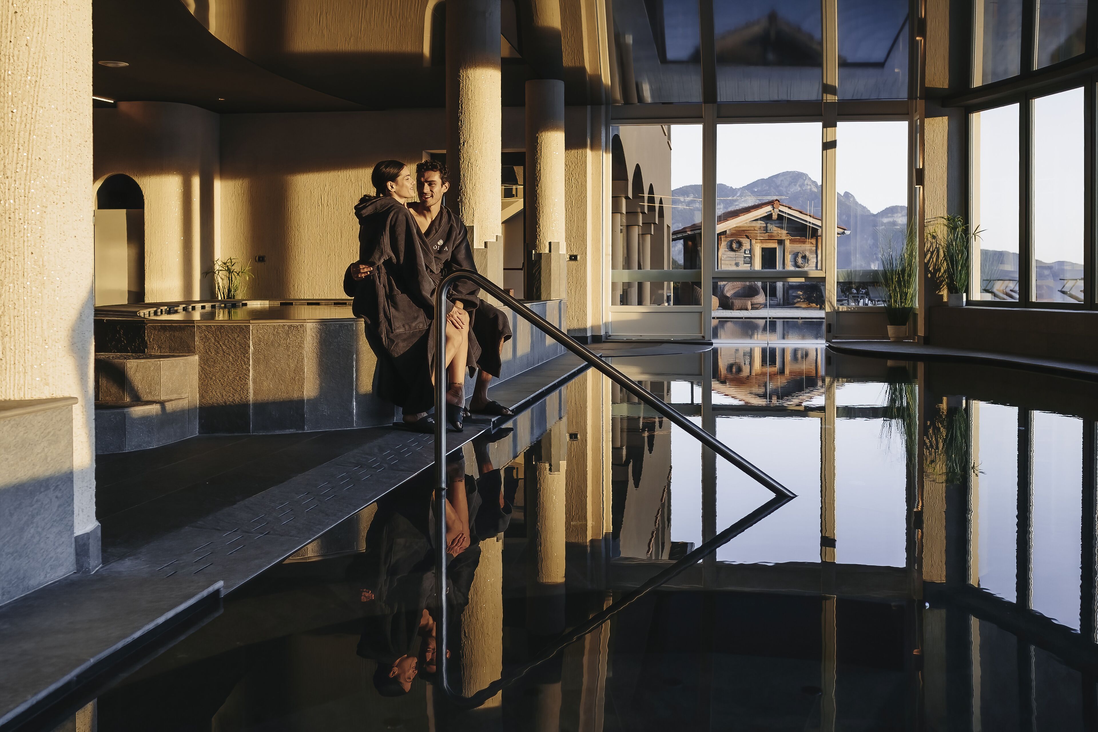 A modern interior with a reflective floor, large windows, and a view of a mountain and building.